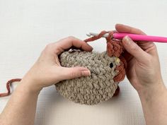 a woman is crocheting a small stuffed animal with pink yarn and scissors in her hands