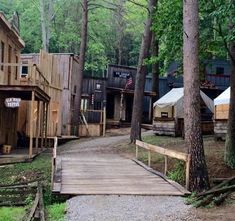 there is a wooden walkway leading to several cabins in the woods with tents on each side