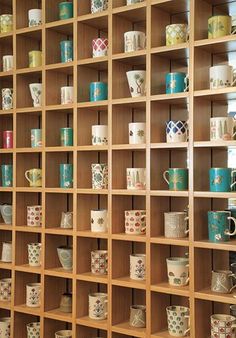 many cups and mugs are on shelves in a room that is filled with wooden shelving