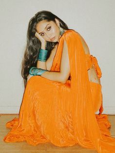 a woman in an orange dress sitting on the floor with her hand under her chin