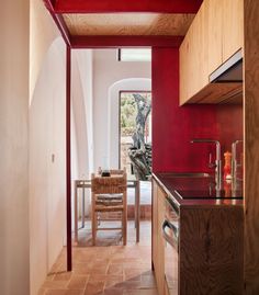 an open kitchen and dining area with red painted walls, tile flooring and wooden cabinets