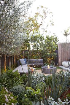 an outdoor seating area is surrounded by greenery and shrubbery, with a fire pit in the middle