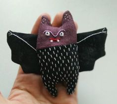 a hand is holding a small bat with eyes and nose, it's made out of fabric