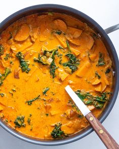 a pan filled with curry and vegetables on top of a white counter next to a wooden spoon