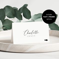 a place card sitting on top of a white plate next to a leafy plant