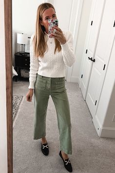 a woman taking a selfie in the mirror while wearing green pants and black shoes