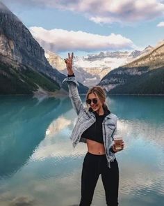 a woman standing on top of a rock next to a lake with mountains in the background