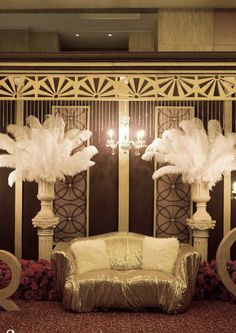 a couch sitting in front of a wall with white feathers on it and chandeliers hanging from the ceiling