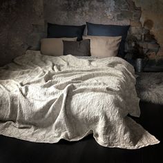 an unmade bed with several pillows and blankets on it, in front of a stone wall