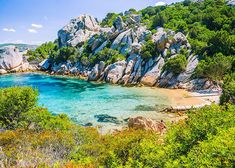 the beach is surrounded by rocks and clear blue water, with green trees around it