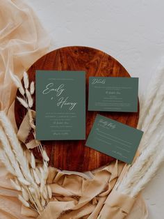 the wedding stationery is laid out on a wooden platter with dried pamodia