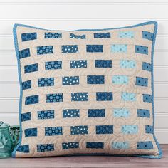 a blue and white quilted pillow sitting on top of a wooden table next to vases