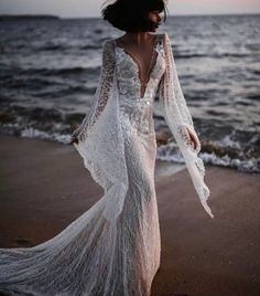 a woman standing on top of a beach next to the ocean wearing a white dress