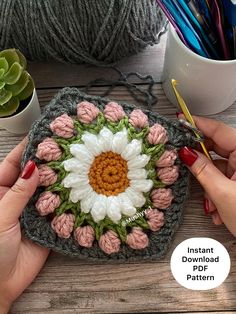 a crocheted flower is being worked on by someone's hands with yarn