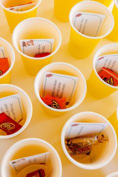 many cups are lined up on the table with their lids down and some candy in them