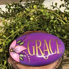 a purple painted rock sitting on top of a tree stump next to some green plants