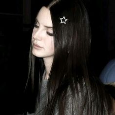 a woman with long hair wearing a pair of stars in her hair, sitting down