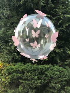 a large bubble filled with pink butterflies floating in front of a lush green park area