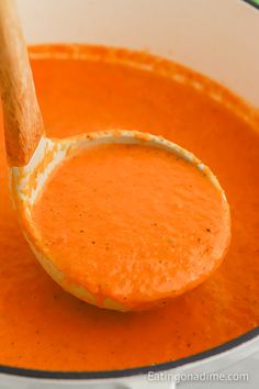 a wooden spoon full of tomato soup in a pot