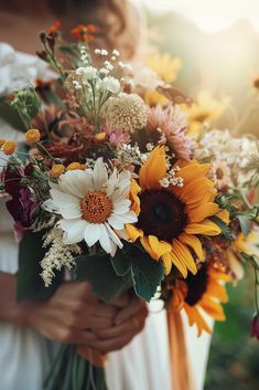 a woman holding a bouquet of sunflowers and other flowers in her hands,