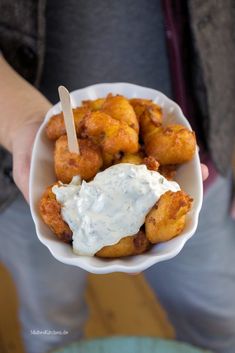 a person holding up a bowl of food with sauce on it and a toothpick sticking out of the top