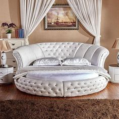 a large white bed sitting on top of a wooden floor next to a window covered in curtains