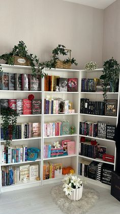 a room with bookshelves filled with lots of books and plants on top of them