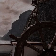 the steering wheel of a ship with mountains in the background