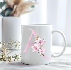 a white coffee mug with pink flowers on it and a monogrammed letter in the middle