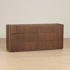 a wooden dresser sitting on top of a hard wood floor next to a white wall