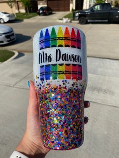 someone is holding up a cup decorated with crayons and glitters on it