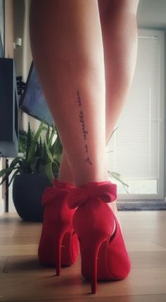 a woman's legs with a tattoo on her left leg and red high heeled shoes