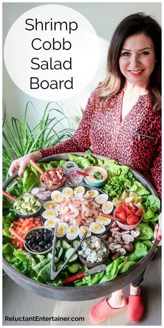 a woman holding a platter full of shrimp, cobb salad and other food items