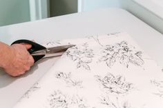 a person cutting fabric with scissors on top of a white tablecloth that has black and white flowers