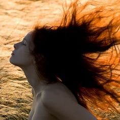 a woman laying in the grass with her hair blowing in the wind and looking up