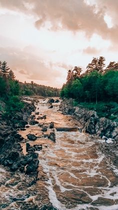 the water is rushing over the rocks in the river at sunset or sunrise, with trees on either side