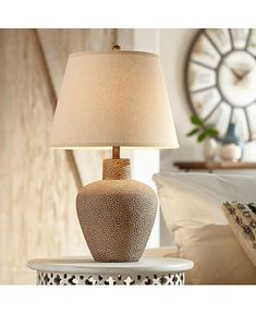 a table lamp sitting on top of a white table next to a pillow and clock