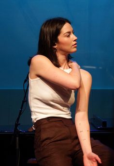 a woman sitting in front of a microphone and wearing a white shirt with brown pants