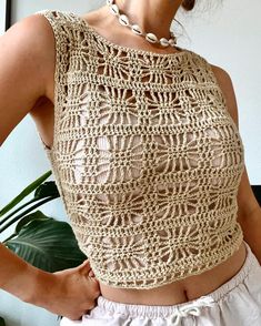 a woman wearing a crochet top and white shorts with her hands on her hips