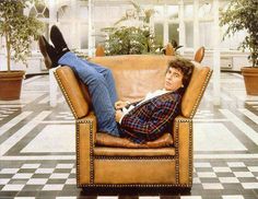 a man laying on top of a brown chair in a room with black and white checkered flooring