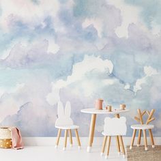 two chairs and a table in front of a wall with clouds painted on it