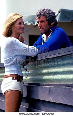 a man and woman standing next to each other in front of a fence with their arms around