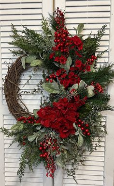 a wreath with red flowers and greenery hanging on a door