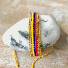 two yellow and red beaded bracelets sitting on top of a rock next to a stone