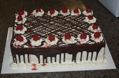 a chocolate cake with white frosting and cherries on top is sitting on a table