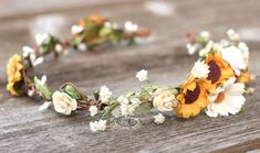 a flower crown is sitting on a wooden table with white and yellow flowers in it