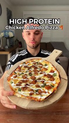 a man holding a pizza on top of a wooden platter in front of him