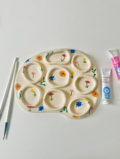 a white tray with flowers painted on it next to paintbrushes and toothpaste