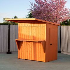 a wooden storage shed sitting on top of a deck next to a tree with purple flowers