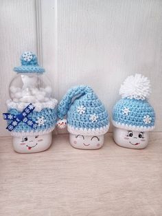 three crocheted snowmen are sitting next to each other in front of a glass jar